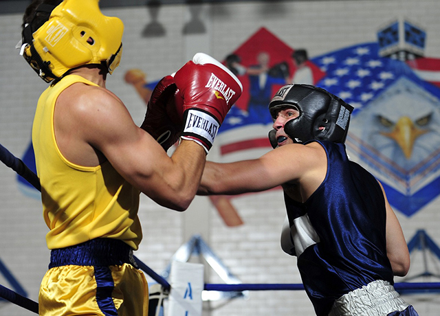 Na zdjęciu widzimy dwóch walczących ze sobą bokserów ubranych w rękawice i kaski bokserskie.